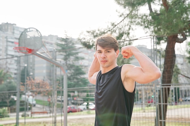 Colocar joven en ropa deportiva haciendo el gesto fuerte en una cancha de baloncesto