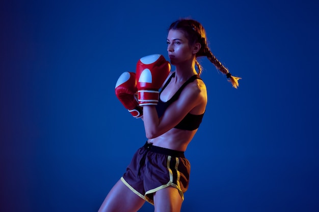 Colocar mujer caucásica en ropa deportiva de boxeo sobre fondo azul de estudio en luz de neón