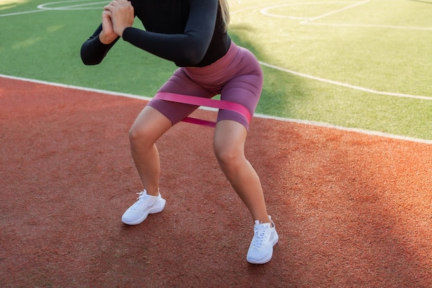 Colocar mujer delgada practicando sentadillas con gomas elásticas de fitness en el estadio