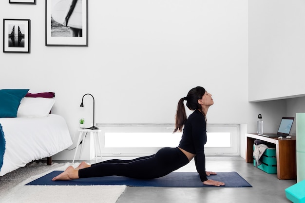 Colocar mujer practicando la pose de Cobra mediante el programa de formación de yoga en línea en el portátil en casa