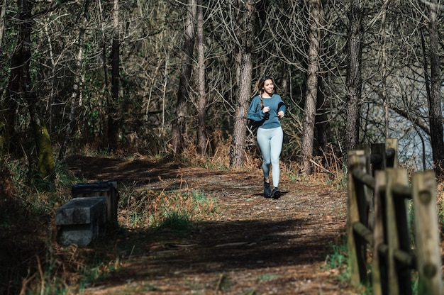 Colocar mujer en ropa deportiva corriendo por sendero en bosque verde