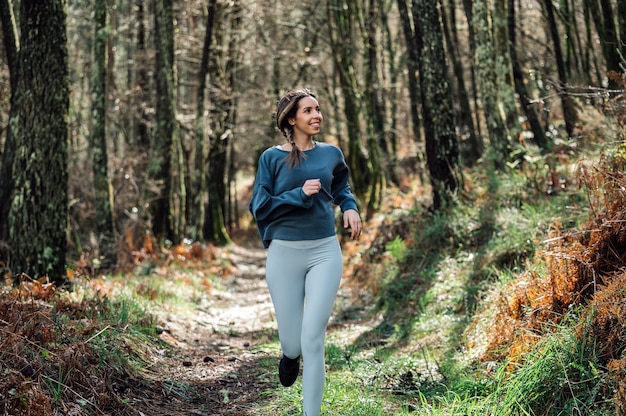 Colocar mujer en ropa deportiva corriendo por sendero en bosque verde