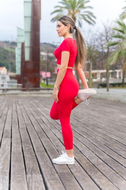 Colocar mujer en traje rojo haciendo estiramientos en un parque de la ciudad fitness y activo saludable