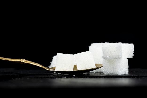 Se colocaron varios terrones de azúcar blanca en una cuchara de latón sobre un fondo de piedra negra.