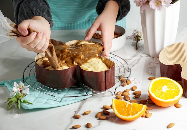 Colomba - traditioneller italienischer Ostertaubenkuchen, Prozess des Dekorierens mit Glasur auf Haselnussbasis, Makaranage, Bestreuen mit Mandeln, Frauenhände.