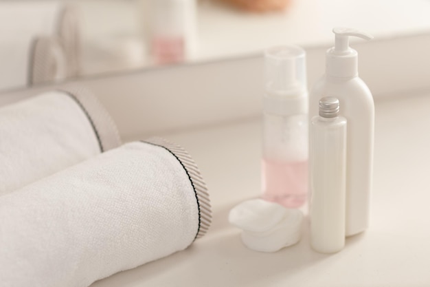 Coloque botellas cosméticas de plástico blanco con jabón en crema y toalla en la mesa blanca en el baño