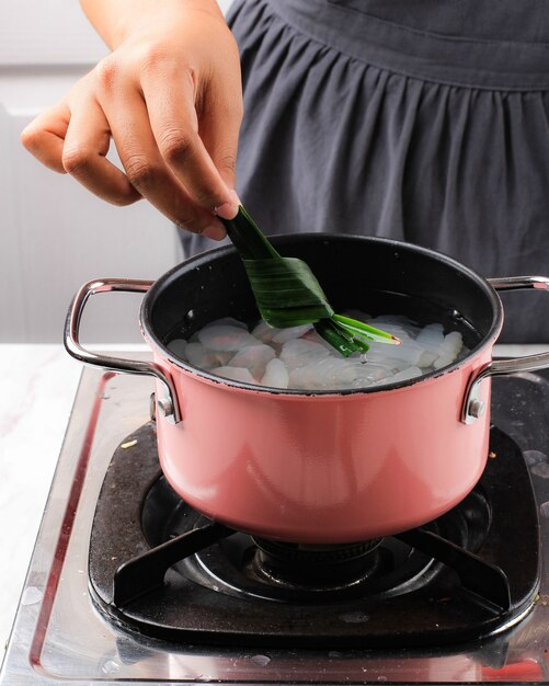 Foto coloque la hoja de pandan en una sartén rosa que contenga fruta de palma de azúcar (kolang kaling). proceso de cocción elaboración de manisan cangkaleng para ramadán desayunando takjil