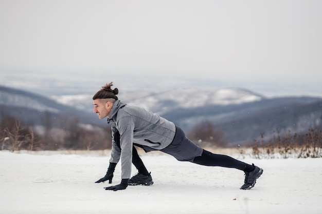 Foto coloque o desportista na posição inicial. esportista fazendo exercícios na neve na natureza. natureza, fitness ao ar livre, fitness de inverno