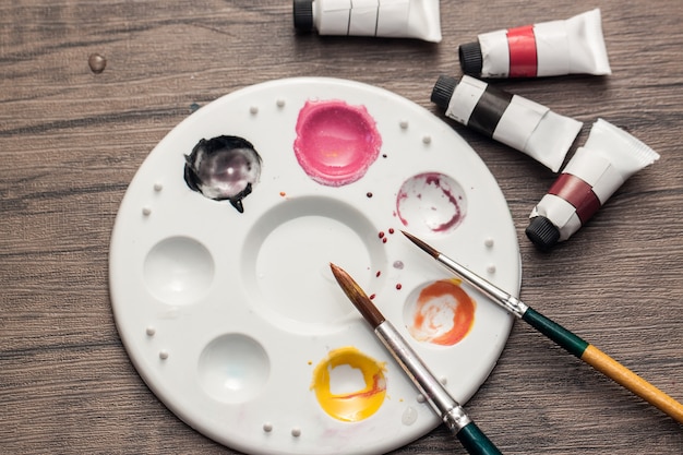 El color del agua y la placa de color mezclado y el pincel se colocan sobre la mesa de madera para dibujar arte en papel.