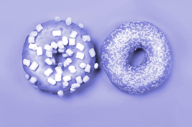 Color del año 2022. Muy Peri. Violeta Dos donuts con glaseado sobre fondo pastel. espacio de copia