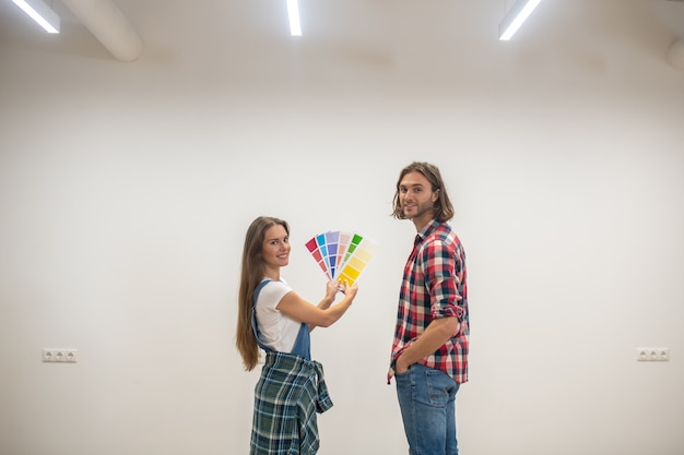 Color de la pared. Mujer joven sosteniendo una paleta de colores y discutiendo el color de las paredes con su novio