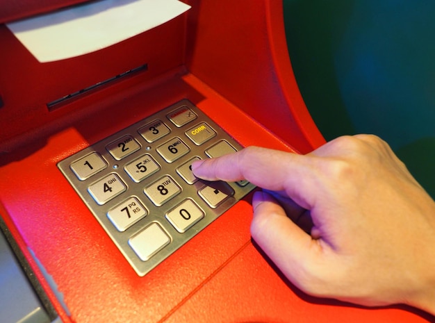 El color rojo del cajero automático y la mano del dedo tocan el botón numérico para la retirada y el primer plano.