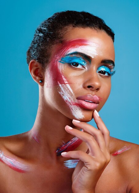 Coloréame intrigado Retrato de estudio de una hermosa joven cubierta de pintura facial posando sobre un fondo azul