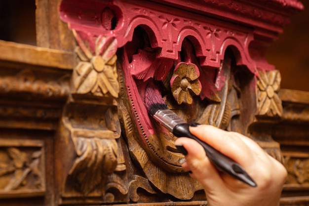 Colorear adornos tallados detallados del viejo aparador de madera buffet con pincel en color rosa con mano femenina en primer plano Nueva vida de cosas viejas Restauración de muebles antiguos