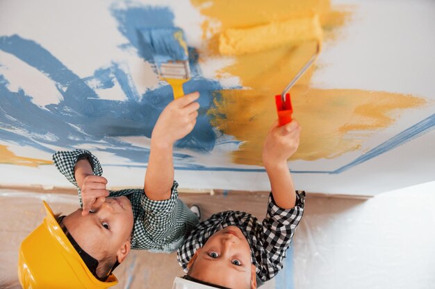 Colores azul y amarillo Dos niños pintando paredes en la habitación doméstica