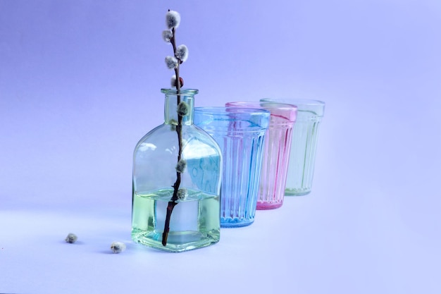 Colores multicolores de primavera, una rama de sauce floreciente en una botella verde, vasos multicolores vacíos, de pie en una fila, espacio de fondo pastel para texto