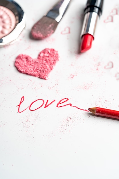 Colorete, pintalabios y lápiz con un corazón y la inscripción amor. Hermoso fondo de cosmética decorativa.