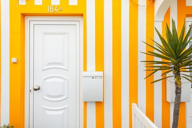 Colorida y hermosa fachada de casa amarilla a rayas con puertas, ventanas, terraza, buzón y palmera en un pueblo de pescadores cerca del océano en Portugal