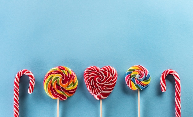 Una colorida línea de deliciosas piruletas de arco iris en palos de madera con fondo azul.