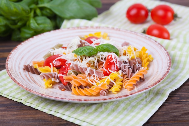 Colorida pasta fusilli con tomate, albahaca y queso sobre una mesa de madera oscura.