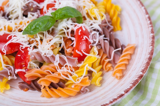 Colorida pasta fusilli con tomate, albahaca y queso sobre una mesa de madera oscura.