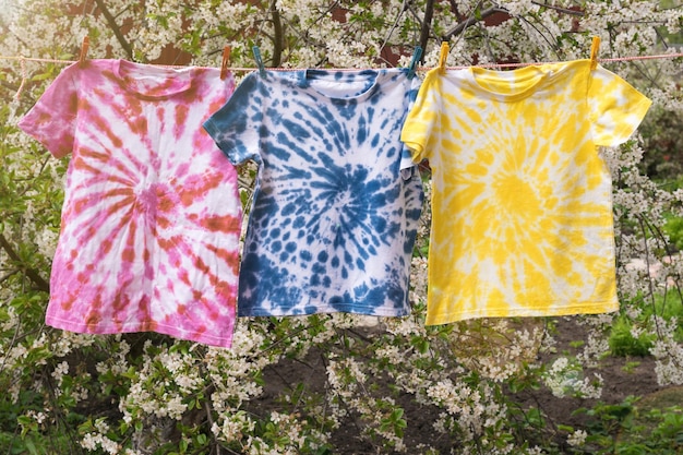 Las coloridas camisetas tie dye se están secando en una cuerda en el jardín de primavera