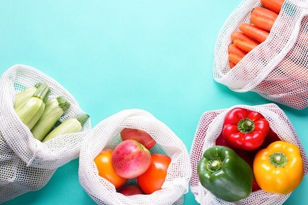 Coloridas frutas y verduras frescas en bolsas de algodón reutilizables sobre fondo azul. Cero desperdicio o concepto responsable de almacenamiento y compra de alimentos. Fondo de marco de estilo de vida sostenible