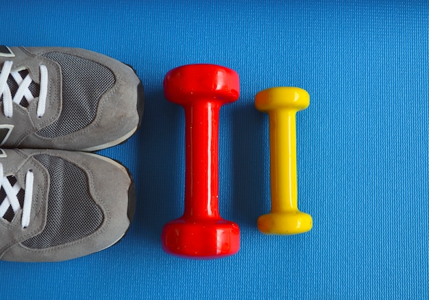 Coloridas pesas, zapatillas de deporte y colchoneta de yoga azul