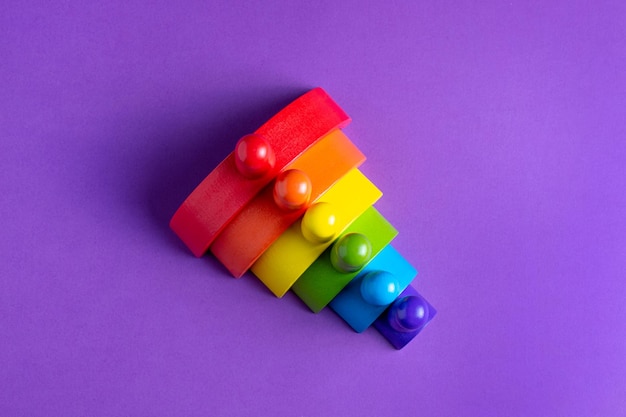 Colorido arco iris de figura humana de madera Waldorf en una pedagogía de enseñanza montessori sobre fondo púrpura concepto de juego infantil