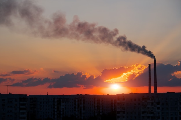 Colorido atardecer mágico. Techos de las casas de la ciudad durante el amanecer. Humo oscuro procedente de la tubería de la central térmica.