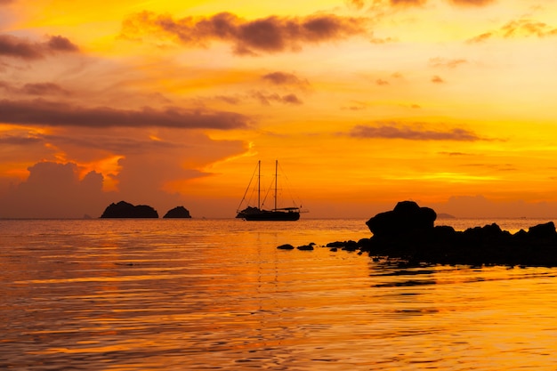 Colorido atardecer en una playa tropical. Naranja puesta de sol en el océano. Colorido atardecer en los trópicos. En el agua hay un velero. Velero silueta con mástiles