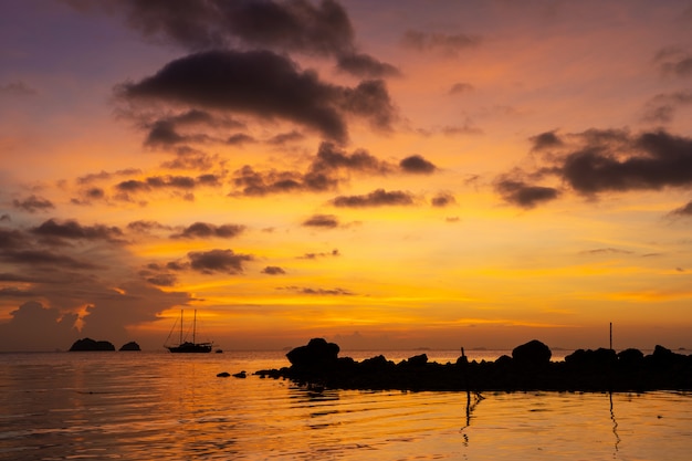 Colorido atardecer en una playa tropical. Naranja puesta de sol en el océano. Colorido atardecer en los trópicos. En el agua hay un velero. Velero silueta con mástiles