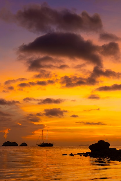 Colorido atardecer en una playa tropical. Naranja puesta de sol en el océano. Colorido atardecer en los trópicos. En el agua hay un velero. Velero silueta con mástiles