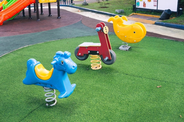 Colorido columpio en forma de caballo para niños en un parque infantil con suelo de césped artificial por la mañana sin gente