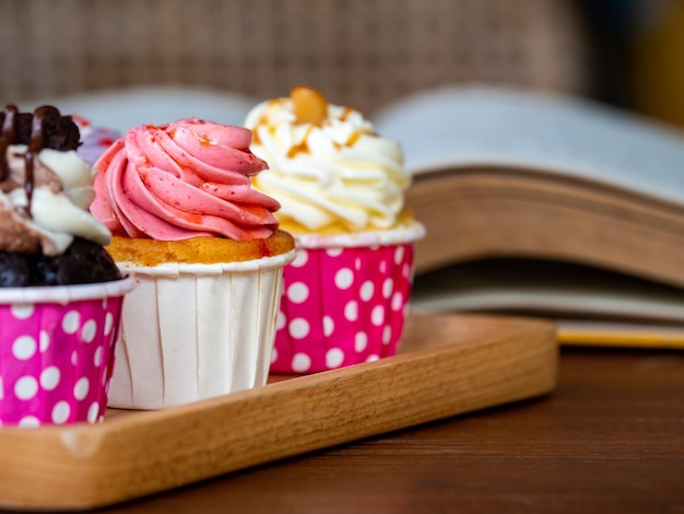 Colorido de cupcake casero en la bandeja de madera y libro abierto en la mesa de madera.