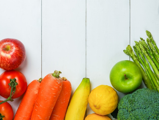 Foto colorido de muitas frutas e legumes no fundo da mesa de madeira branca