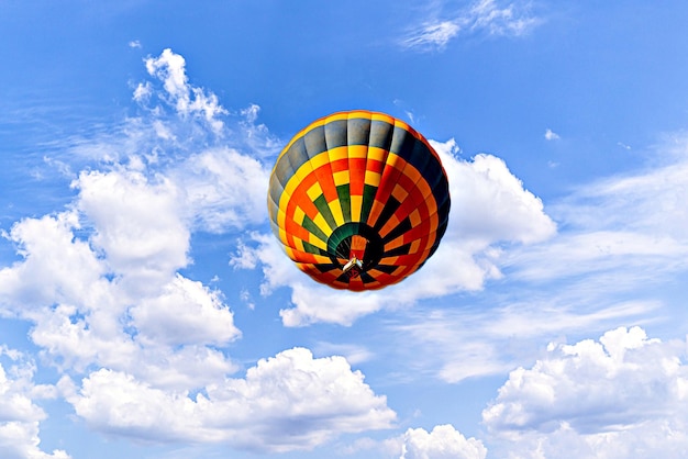 Un colorido globo aerostático volando sobre el cielo azul con nubes blancas