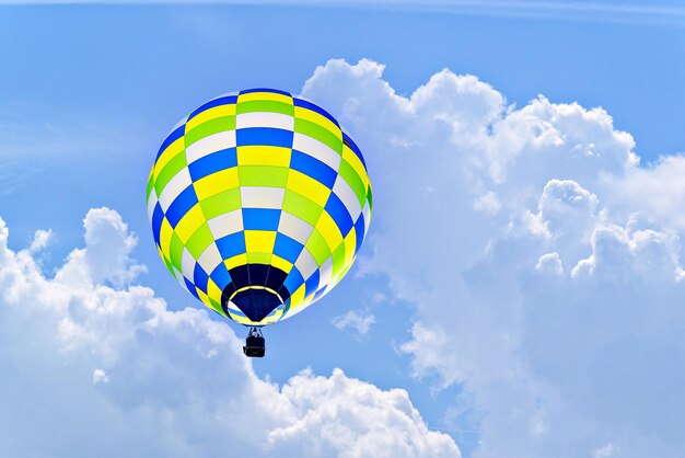 Un colorido globo aerostático volando sobre el cielo azul con nubes blancas