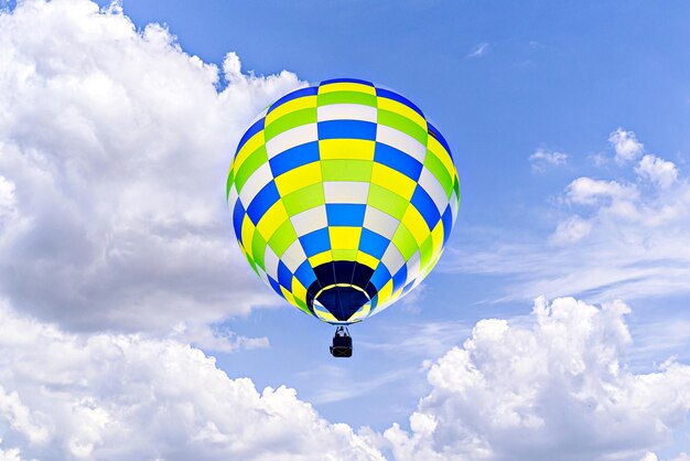 Un colorido globo aerostático volando sobre el cielo azul con nubes blancas