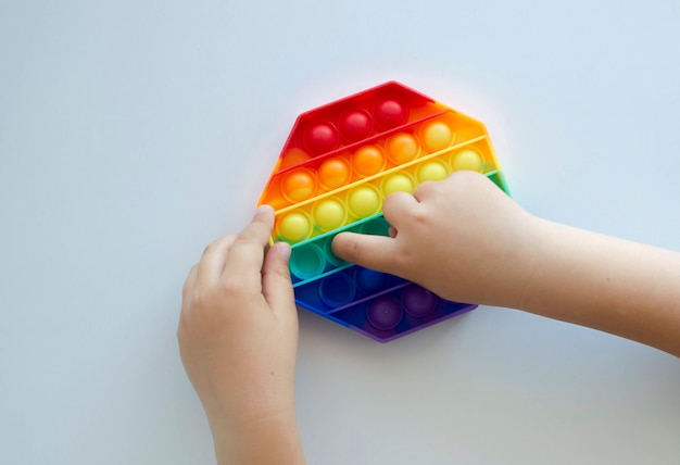 Colorido juguete sensorial antiestrés fidget push pop en manos de los niños. Niño jugando con arco iris pop, vista superior Nuevo juguete antiestrés para niños y adultos.