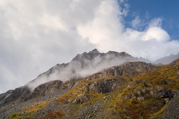 Colorido paisaje alpino con montañas rocosas en nubes bajas de baile a la luz del sol de la mañana. Paisaje de montaña con rocas afiladas entre espesas nubes bajas. Impresionante vista a las altas montañas rocosas con poca nubosidad.