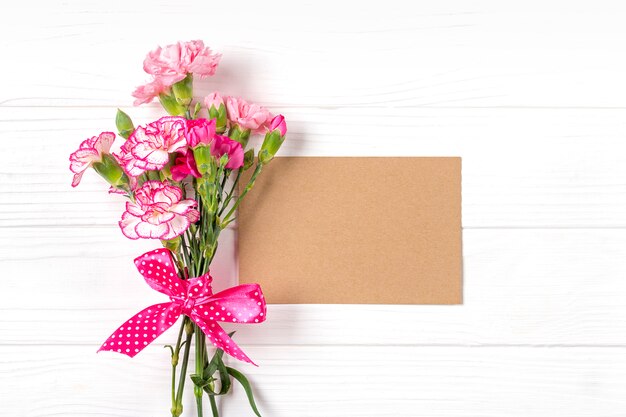 Colorido ramo de diferentes flores de clavel rosa, cuaderno blanco sobre fondo blanco de madera