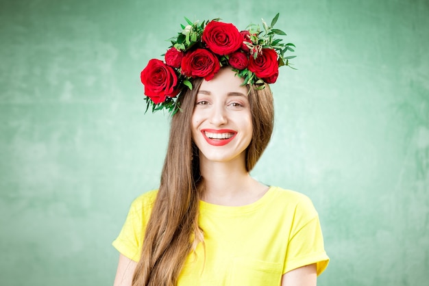 Colorido retrato de una bella mujer en camiseta amarilla con corona de rosas rojas sobre fondo verde