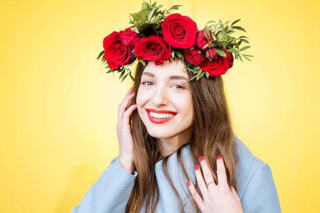 Colorido retrato de una hermosa mujer en abrigo azul con corona de rosas rojas sobre fondo amarillo