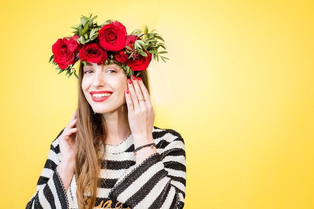 Colorido retrato de una hermosa mujer en suéter con corona de rosas rojas sobre fondo amarillo