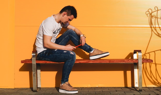 Colorido retrato de un hombre guapo en camiseta blanca y jeans con teléfono sobre fondo amarillo