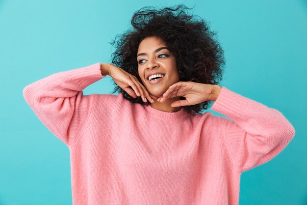 Colorido retrato de mujer joven de 20 años con peinado afro sonriendo y mirando a un lado cogidos de la mano en la cara, aislado sobre la pared azul