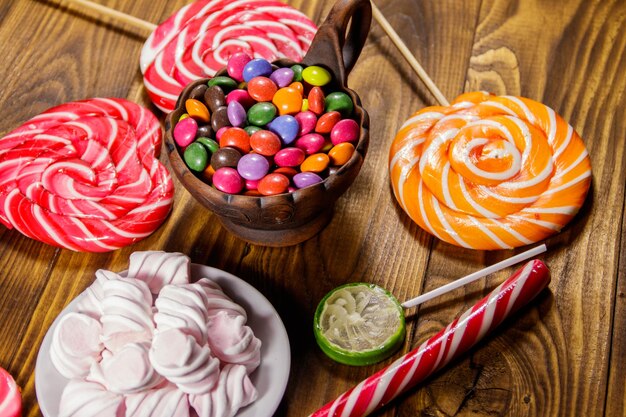 Coloridos caramelos de chocolate, piruletas, bastón de caramelo y malvaviscos en la mesa de madera