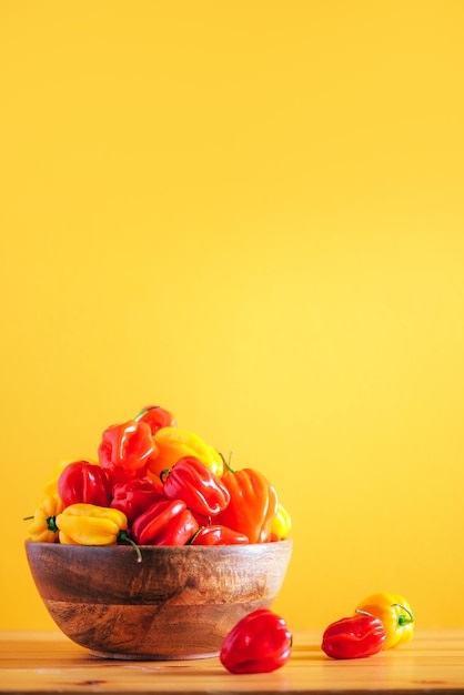 Coloridos chiles scotch bonnet en tazón de madera sobre fondo naranja Copiar espacio