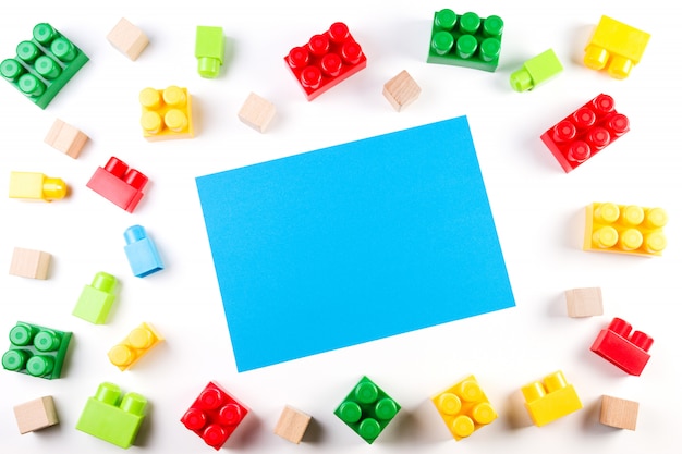 Coloridos cubos de madera y bloques de construcción de plástico con tarjeta de papel en blanco azul sobre blanco